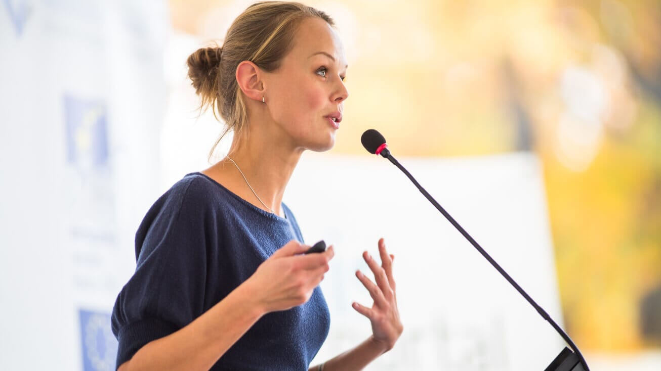 Woman talking into long microphone at podium